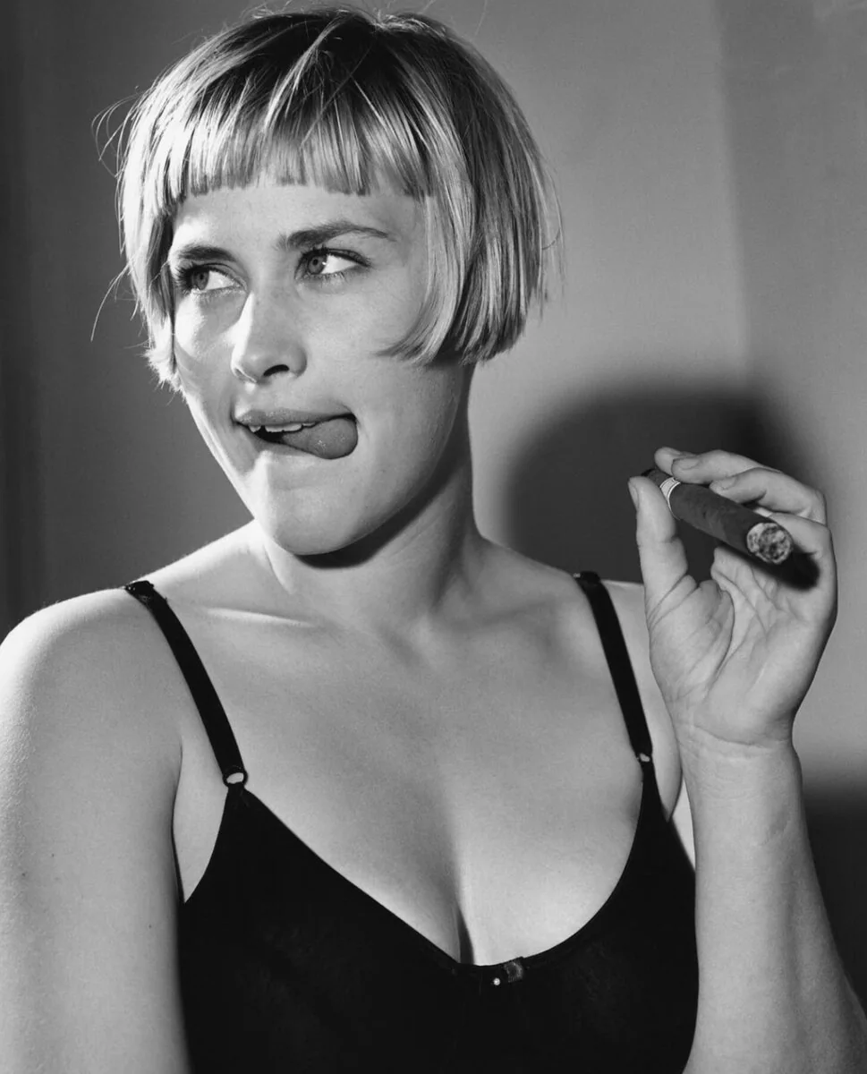 Patricia Arquette in a black strappy top holding a cigar in a black-and-white portrait by Bruce Weber, 1992