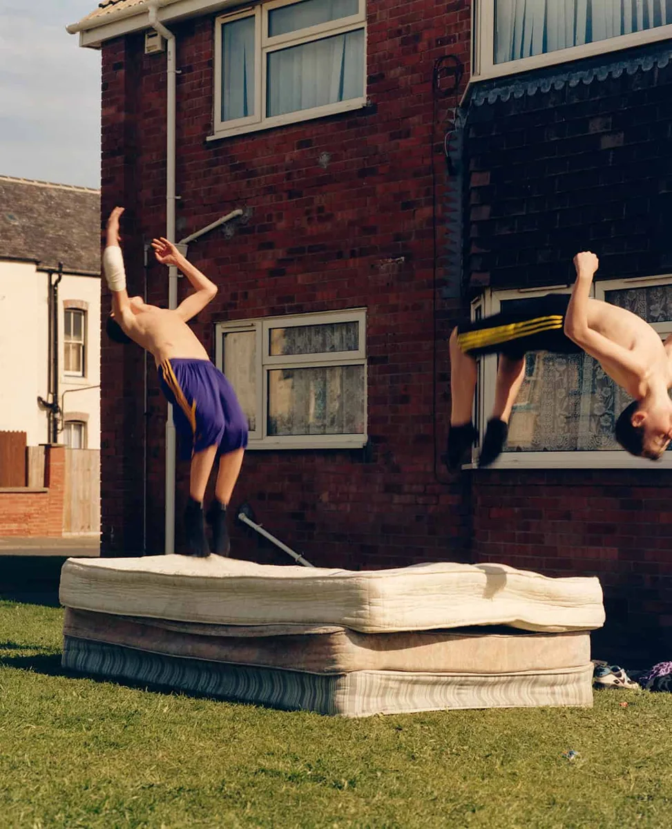 Two young people jumping on stacked mattresses in a garden, from The British Isles by Jamie Hawkesworth