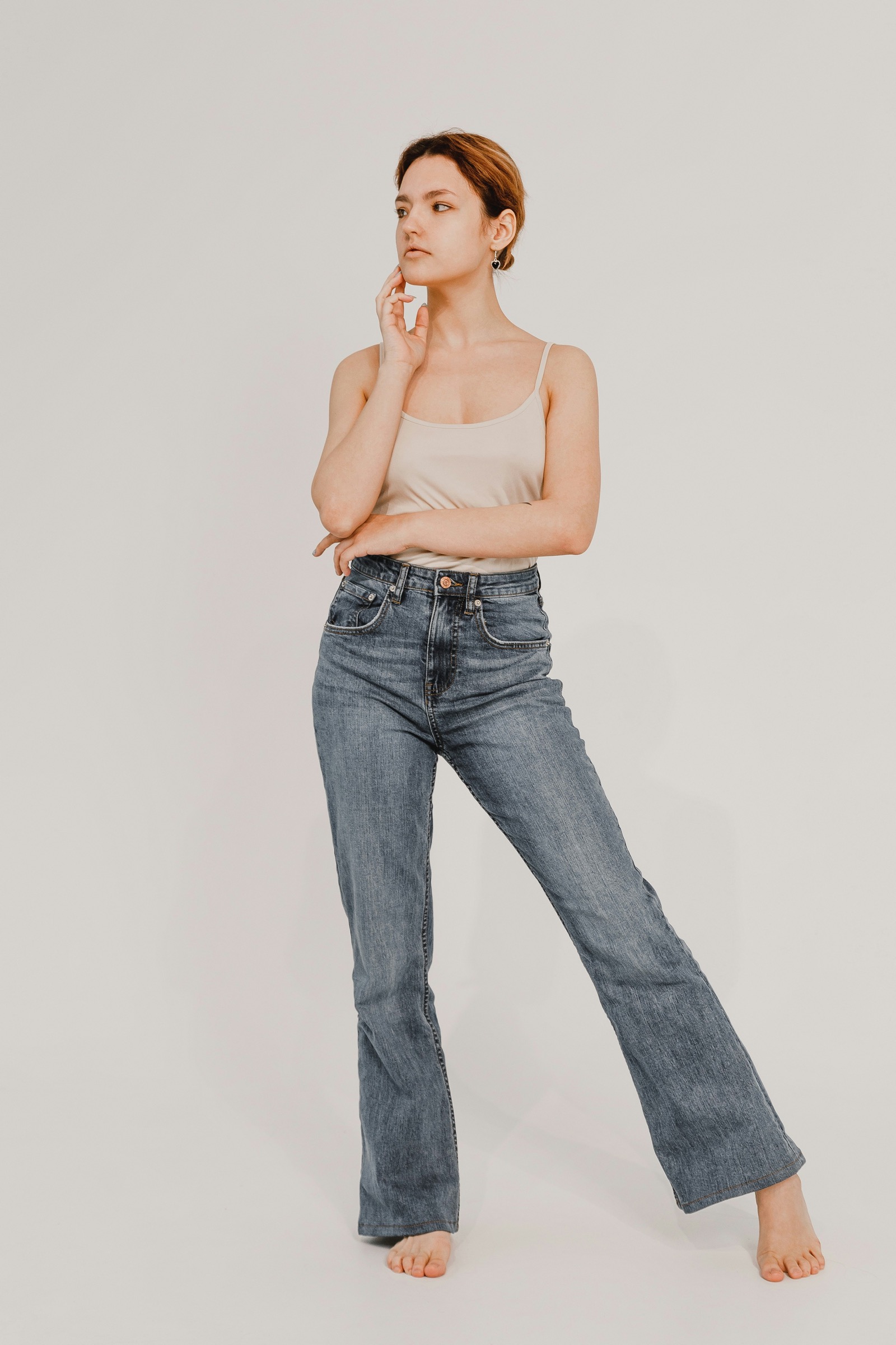 Model in schlichtem beigefarbenem Top und Jeans vor neutralem Studiohintergrund